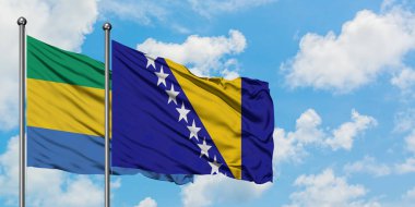 Gabon ve Bosna Hersek bayrağı birlikte beyaz bulutlu mavi gökyüzüne karşı rüzgarda sallayarak. Diplomasi kavramı, uluslararası ilişkiler.