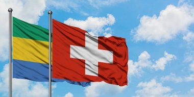 Gabon ve İsviçre bayrağı birlikte beyaz bulutlu mavi gökyüzüne karşı rüzgarda sallayarak. Diplomasi kavramı, uluslararası ilişkiler.