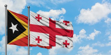 Doğu Timor ve Gürcistan bayrağı birlikte beyaz bulutlu mavi gökyüzüne karşı rüzgarda sallayarak. Diplomasi kavramı, uluslararası ilişkiler.