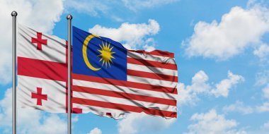 Gürcistan ve Malezya bayrağı birlikte beyaz bulutlu mavi gökyüzüne karşı rüzgarda sallayarak. Diplomasi kavramı, uluslararası ilişkiler.