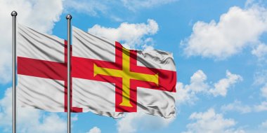 İngiltere ve Guernsey bayrağı birlikte beyaz bulutlu mavi gökyüzüne karşı rüzgarda sallayarak. Diplomasi kavramı, uluslararası ilişkiler.
