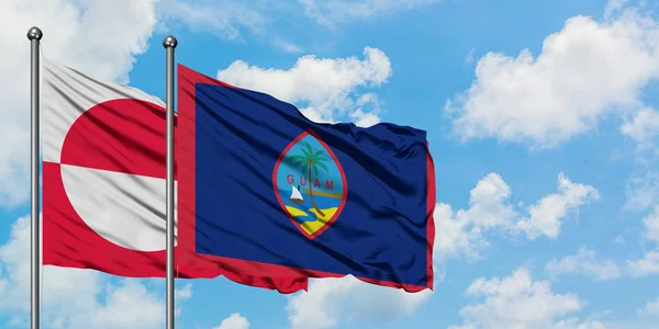 Bandera de Groenlandia y Guam ondeando en el viento contra el cielo azul nublado blanco juntos. Concepto diplomático, relaciones internacionales . — Foto de Stock