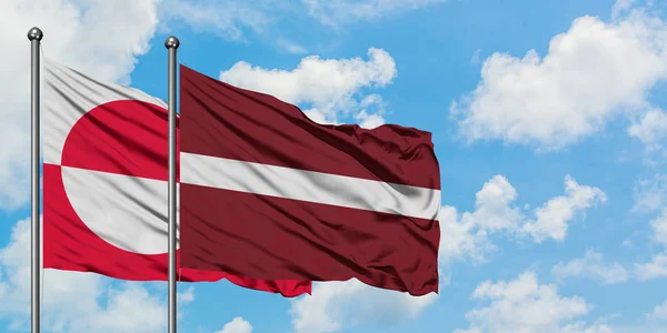 Grönland och Lettland flagga vifta i vinden mot vit grumlig blå himmel tillsammans. Diplomatisk koncept, internationella relationer. — Stockfoto
