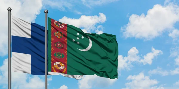 Bandera de Finlandia y Turkmenistán ondeando en el viento contra el cielo azul nublado blanco juntos. Concepto diplomático, relaciones internacionales . — Foto de Stock
