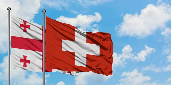 Gruzie a Švýcarsko vlají ve větru proti bíle zatažené modré obloze. Diplomacie, mezinárodní vztahy. — Stock fotografie
