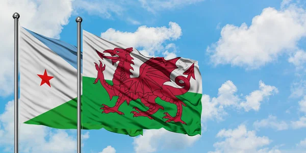 Djibuti e a bandeira do País de Gales agitando no vento contra o céu azul nublado branco juntos. Conceito de diplomacia, relações internacionais . — Fotografia de Stock