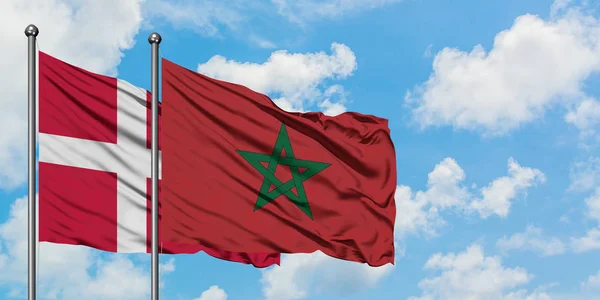 Bandera de Dinamarca y Marruecos ondeando en el viento contra el cielo azul nublado blanco juntos. Concepto diplomático, relaciones internacionales . — Foto de Stock