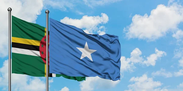 Bandera de Dominica y Somalia ondeando en el viento contra el cielo azul nublado blanco juntos. Concepto diplomático, relaciones internacionales . — Foto de Stock