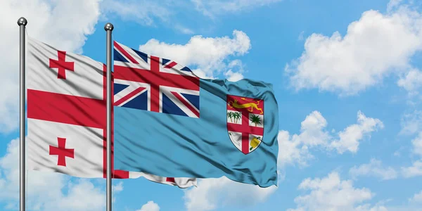 Bandera de Georgia y Fiyi ondeando en el viento contra el cielo azul nublado blanco juntos. Concepto diplomático, relaciones internacionales . —  Fotos de Stock