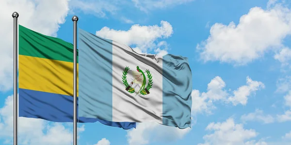 Gabon e Guatemala sventolano bandiera nel vento contro bianco cielo blu nuvoloso insieme. Concetto di diplomazia, relazioni internazionali . — Foto Stock