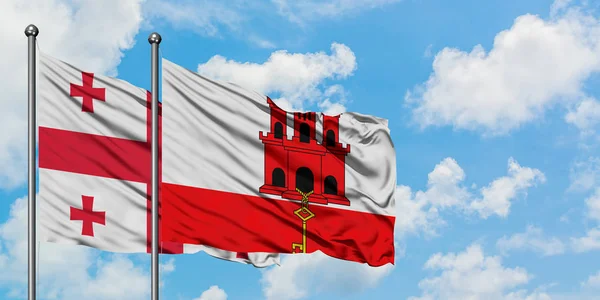 Bandera de Georgia y Gibraltar ondeando en el viento contra el cielo azul nublado blanco juntos. Concepto diplomático, relaciones internacionales . — Foto de Stock
