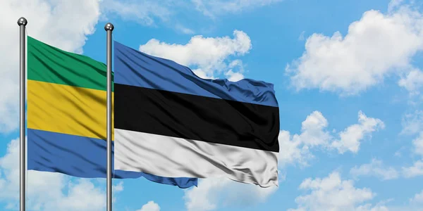 加蓬和爱沙尼亚国旗在风中飘扬，与白云相间的蓝天相一起。外交概念、国际关系. — 图库照片