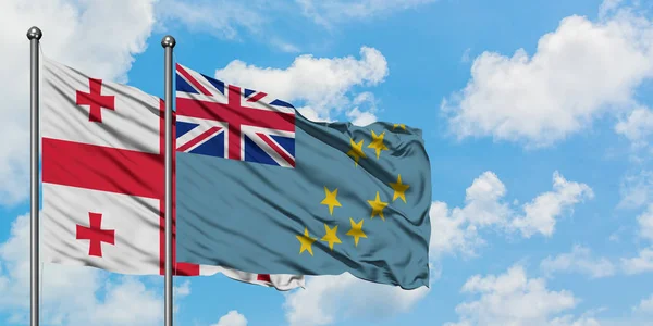 Bandera de Georgia y Tuvalu ondeando en el viento contra el cielo azul nublado blanco juntos. Concepto diplomático, relaciones internacionales . — Foto de Stock