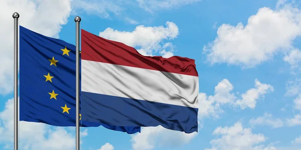 Bandera de la Unión Europea y los Países Bajos ondeando en el viento contra el cielo azul nublado blanco juntos. Concepto diplomático, relaciones internacionales . — Foto de Stock