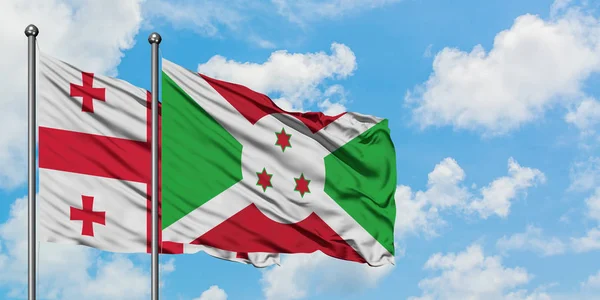Bandera de Georgia y Burundi ondeando en el viento contra el cielo azul nublado blanco juntos. Concepto diplomático, relaciones internacionales . — Foto de Stock