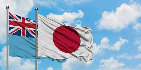 Fidzsi-szigetek és Japán zászló integetett a szél ellen, fehér felhős kék ég együtt. Diplomáciai koncepció, nemzetközi kapcsolatok. — Stock Fotó
