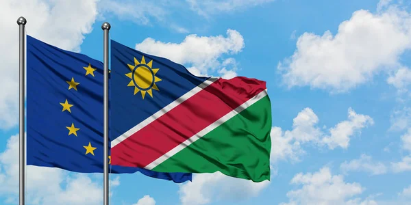 Bandera de la Unión Europea y Namibia ondeando en el viento contra el cielo azul nublado blanco juntos. Concepto diplomático, relaciones internacionales . — Foto de Stock