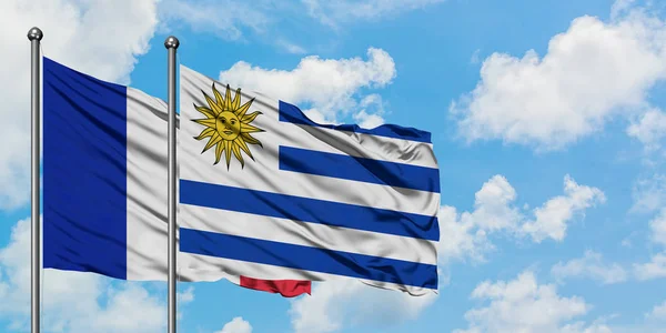 Frankreich und Uruguay wehen gemeinsam im Wind vor dem wolkenverhangenen blauen Himmel. Diplomatie-Konzept, internationale Beziehungen. — Stockfoto