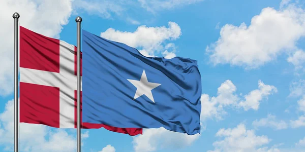 Bandera de Dinamarca y Somalia ondeando en el viento contra el cielo azul nublado blanco juntos. Concepto diplomático, relaciones internacionales . — Foto de Stock