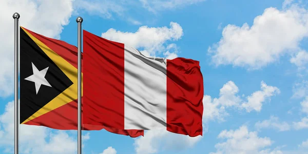Timor Oriental y la bandera del Perú ondeando en el viento contra el cielo azul nublado blanco juntos. Concepto diplomático, relaciones internacionales . —  Fotos de Stock