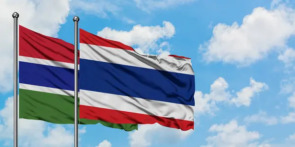 Gâmbia e Tailândia acenando com o vento contra o céu azul nublado branco juntos. Conceito de diplomacia, relações internacionais . — Fotografia de Stock