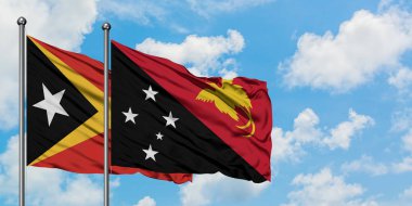 Doğu Timor ve Papua Yeni Gine bayrağı birlikte beyaz bulutlu mavi gökyüzüne karşı rüzgarda sallayarak. Diplomasi kavramı, uluslararası ilişkiler.