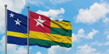 Curacao ve Togo bayrağı birlikte beyaz bulutlu mavi gökyüzüne karşı rüzgarda sallayarak. Diplomasi kavramı, uluslararası ilişkiler.