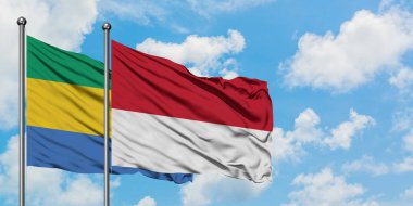 Gabon ve Monako bayrağı birlikte beyaz bulutlu mavi gökyüzüne karşı rüzgarda sallayarak. Diplomasi kavramı, uluslararası ilişkiler.