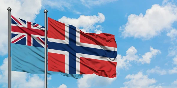 Bandera de Fiyi y Noruega ondeando en el viento contra el cielo azul nublado blanco juntos. Concepto diplomático, relaciones internacionales . — Foto de Stock