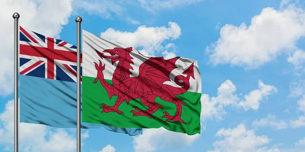 一緒に白い曇り青い空に対して風に手を振るフィジーとウェールズの旗。外交概念、国際関係. — ストック写真