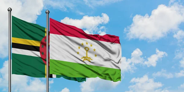 Bandera de Dominica y Tayikistán ondeando en el viento contra el cielo azul nublado blanco juntos. Concepto diplomático, relaciones internacionales . — Foto de Stock