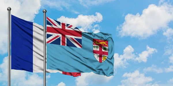 Bandera de Francia y Fiyi ondeando en el viento contra el cielo azul nublado blanco juntos. Concepto diplomático, relaciones internacionales . — Foto de Stock