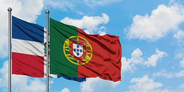 Bandera de República Dominicana y Portugal ondeando en el viento contra el cielo azul nublado blanco juntos. Concepto diplomático, relaciones internacionales . — Foto de Stock