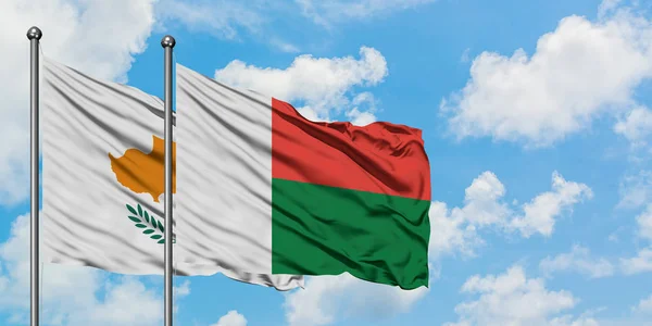 Bandera de Chipre y Madagascar ondeando en el viento contra el cielo azul nublado blanco juntos. Concepto diplomático, relaciones internacionales . — Foto de Stock