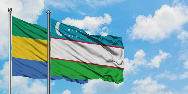 ガボンとウズベキスタンの旗は、一緒に白い曇り青い空に対して風に手を振る。外交概念、国際関係. — ストック写真