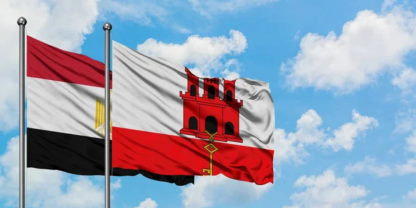 Bandera de Egipto y Gibraltar ondeando en el viento contra el cielo azul nublado blanco juntos. Concepto diplomático, relaciones internacionales . — Foto de Stock