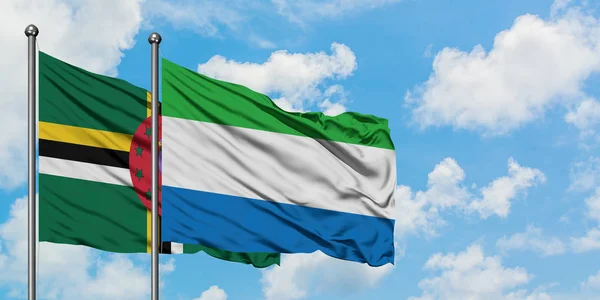 Dominica a Sierra Leone vlají ve větru proti bíle zatažené modré obloze. Diplomacie, mezinárodní vztahy. — Stock fotografie