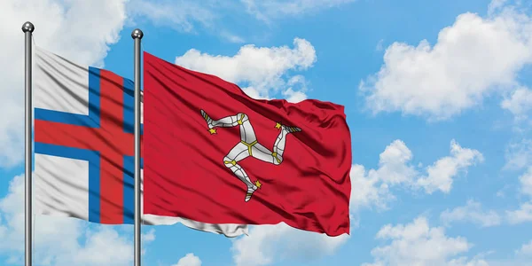 Islas Feroe y la bandera de la Isla de Man ondeando en el viento contra el cielo azul nublado blanco juntos. Concepto diplomático, relaciones internacionales . — Foto de Stock