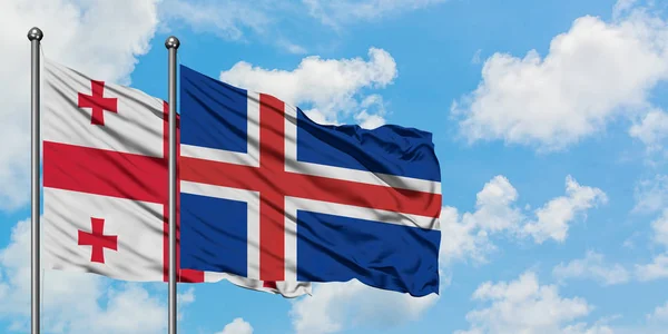 Bandera de Georgia e Islandia ondeando en el viento contra el cielo azul nublado blanco juntos. Concepto diplomático, relaciones internacionales . — Foto de Stock