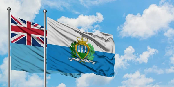 Bandera de Fiji y San Marino ondeando en el viento contra el cielo azul nublado blanco juntos. Concepto diplomático, relaciones internacionales . — Foto de Stock