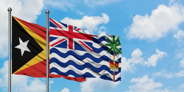 Kelet-Timor és a brit indiai-óceáni terület zászló integetett a szél ellen, fehér felhős kék ég együtt. Diplomáciai koncepció, nemzetközi kapcsolatok. — Stock Fotó