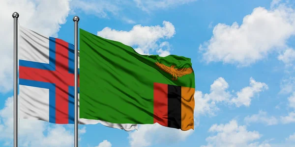 Bandera de las Islas Feroe y Zambia ondeando en el viento contra el cielo azul nublado blanco juntos. Concepto diplomático, relaciones internacionales . — Foto de Stock