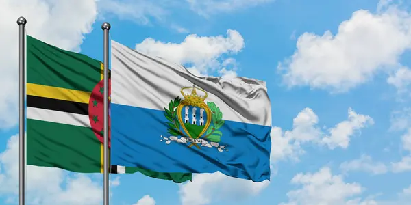 Dominica y la bandera de San Marino ondeando en el viento contra el cielo azul nublado blanco juntos. Concepto diplomático, relaciones internacionales . — Foto de Stock