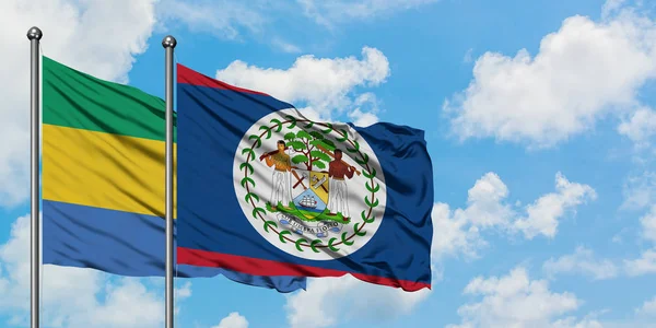 Bandera de Gabón y Belice ondeando en el viento contra el cielo azul nublado blanco juntos. Concepto diplomático, relaciones internacionales . — Foto de Stock