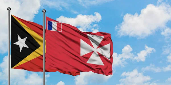 Timor Oriental y Wallis y la bandera de Futuna ondeando en el viento contra el cielo azul nublado blanco juntos. Concepto diplomático, relaciones internacionales . — Foto de Stock