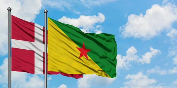 Bandera de Dinamarca y Guayana Francesa ondeando en el viento contra el cielo azul nublado blanco juntos. Concepto diplomático, relaciones internacionales . — Foto de Stock