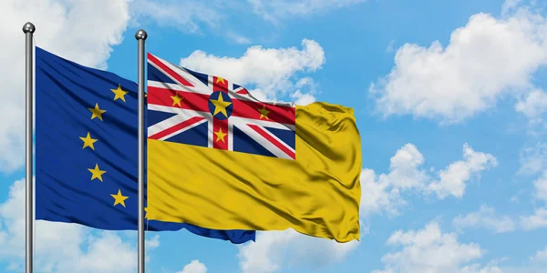 Bandera de la Unión Europea y Niue ondeando en el viento contra el cielo azul nublado blanco juntos. Concepto diplomático, relaciones internacionales . — Foto de Stock