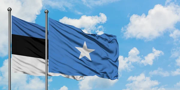 Bandera de Estonia y Somalia ondeando en el viento contra el cielo azul nublado blanco juntos. Concepto diplomático, relaciones internacionales . — Foto de Stock
