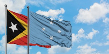 Doğu Timor ve Mikronezya bayrağı birlikte beyaz bulutlu mavi gökyüzüne karşı rüzgarda sallayarak. Diplomasi kavramı, uluslararası ilişkiler.