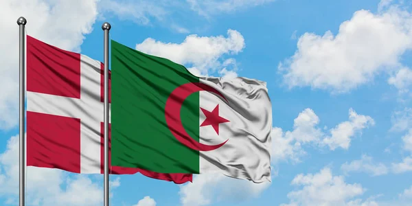 Bandera de Dinamarca y Argelia ondeando en el viento contra el cielo azul nublado blanco juntos. Concepto diplomático, relaciones internacionales . — Foto de Stock